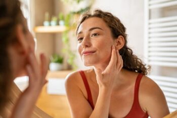 Young woman examining skin in bathroom mirror