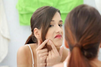 Woman squeezing pimple in bathroom mirror